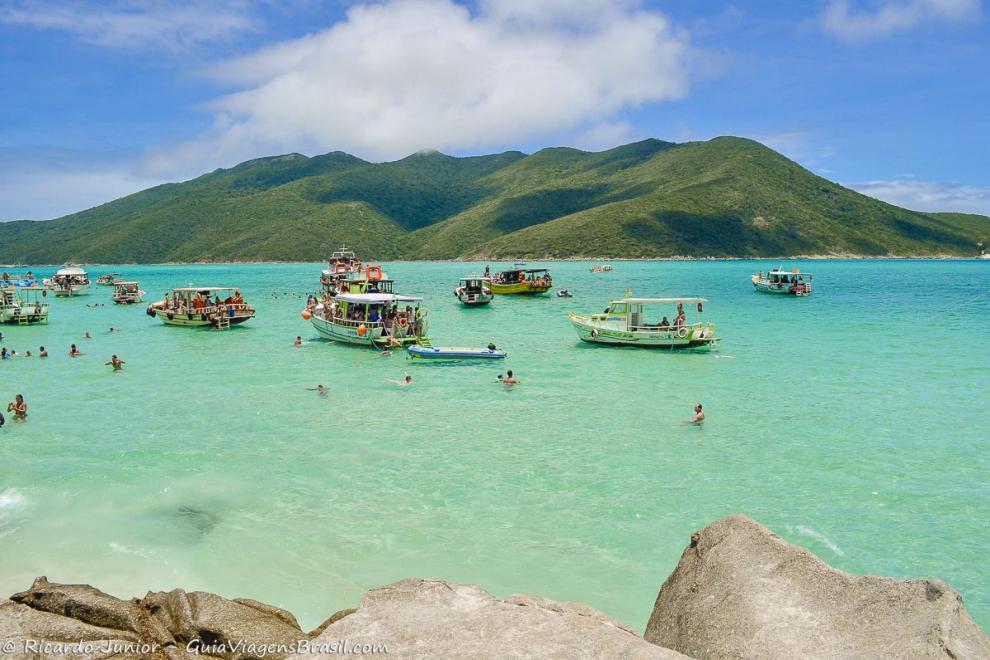 Imagem do mar transparentes da praia e ao fundo lindos morros.